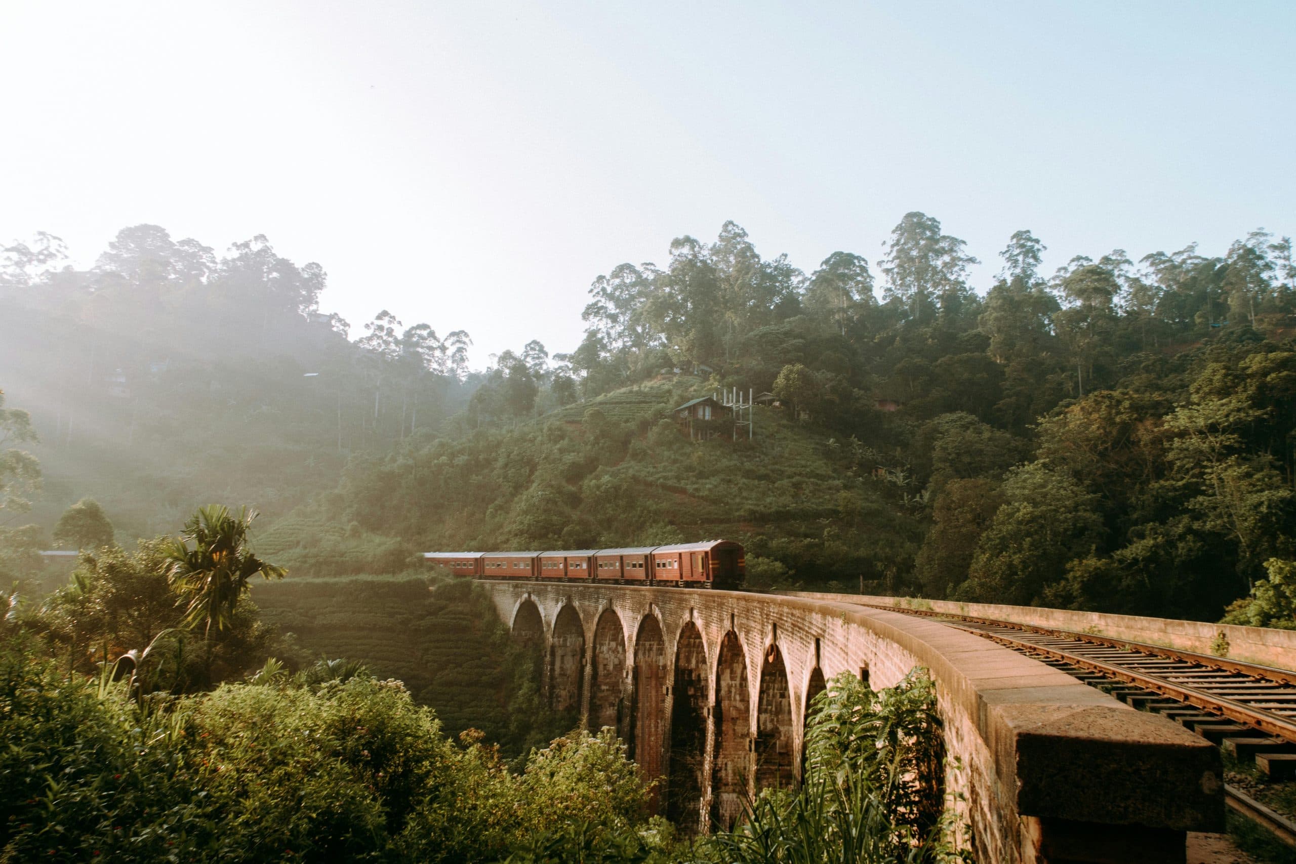 Train crossing Nine Arch Bridge near Ella, Sri Lanka, with misty forest and hills behind